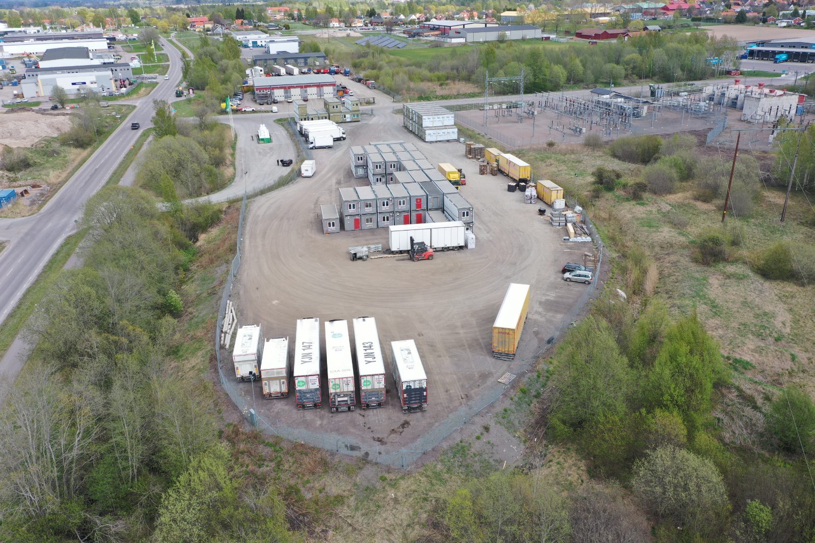Flygbild över en inhägnad upplagsyta med trailers, moduler och material uppställda på hårdgjord mark